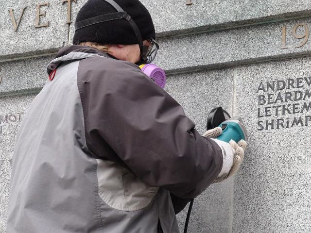 a man wearing a gas mask is working on a stone wall that says andrew beardm letkem shrimp