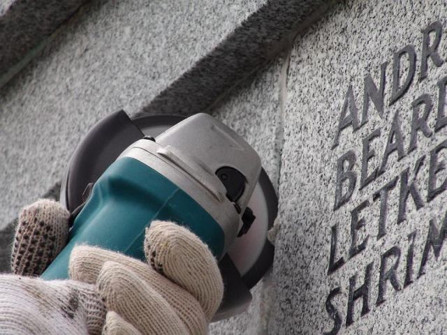 a person is using a grinder to remove a name from a stone wall