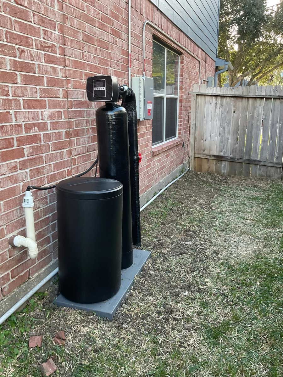 Black water softener tank and utility equipment beside a brick house outdoors