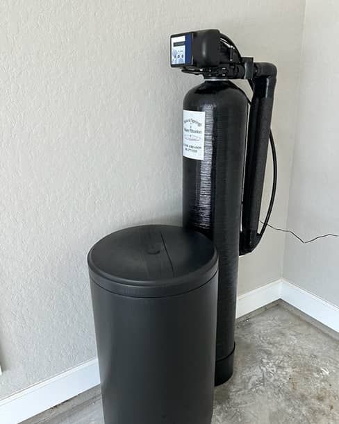 Black water softener and brine tank in a corner on a concrete floor.