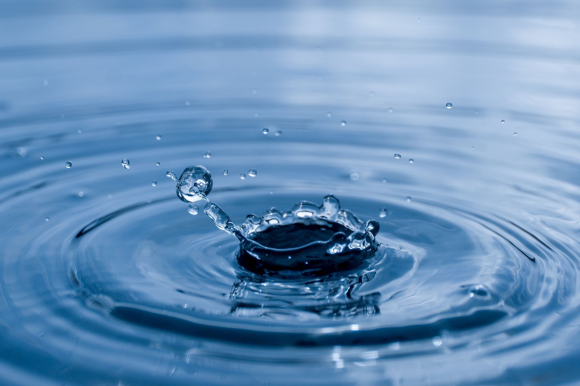 Water droplet splashing into a calm blue surface, creating ripples