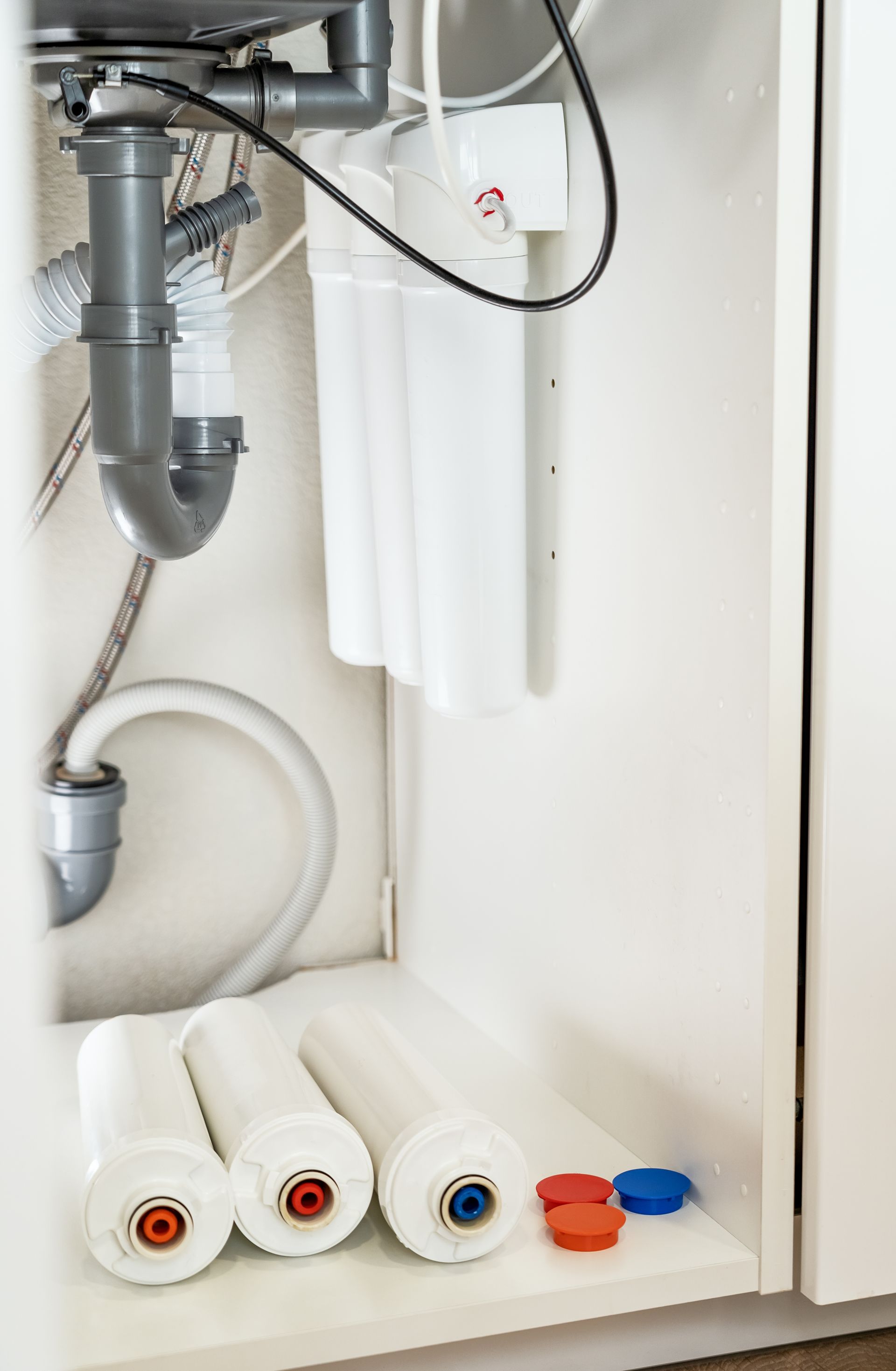 Open under-sink cabinet with plumbing and water filters on the bottom shelf.