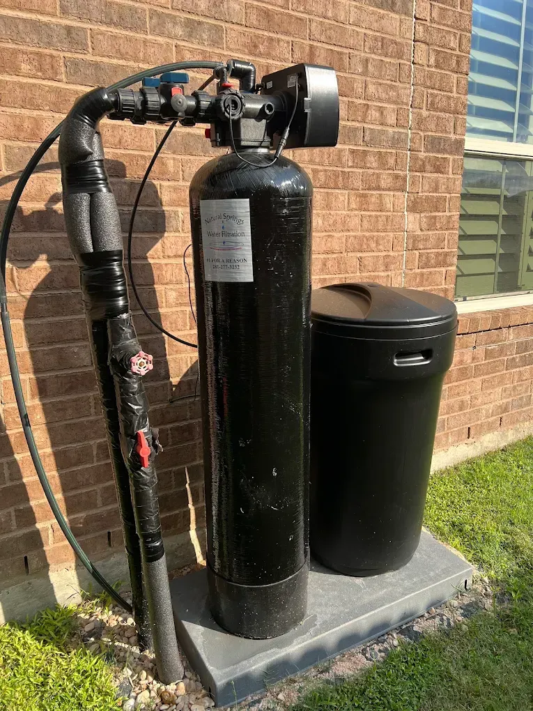 Two black water treatment tanks beside a brick house on a concrete pad