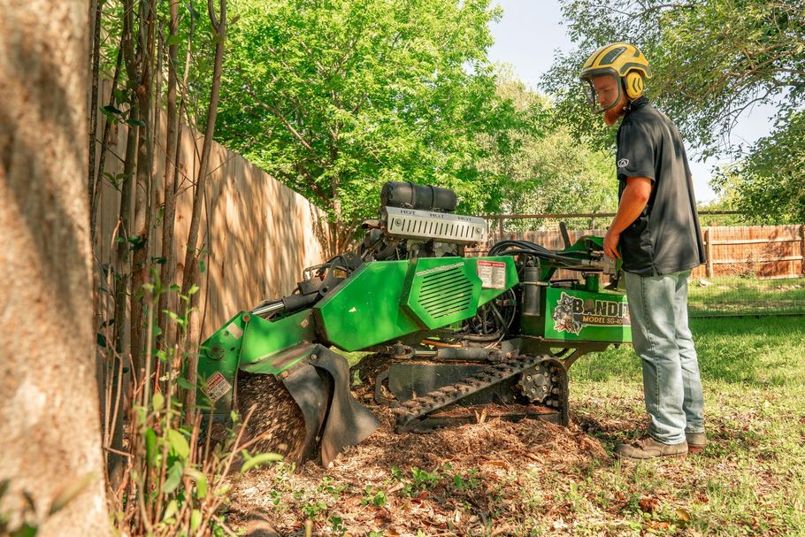 Person operating a green wood chipper beside a fence in a wooded yard