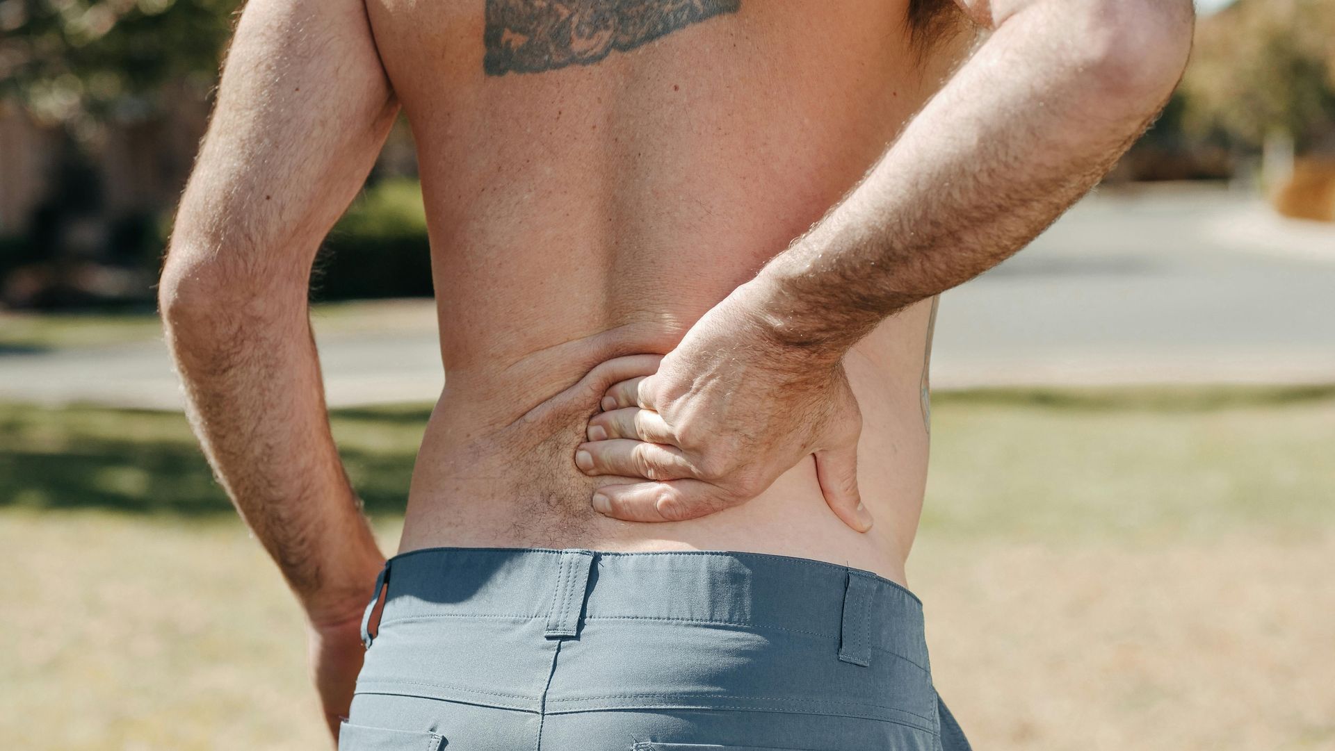 Man with bare torso, holding lower back in pain, outdoors.