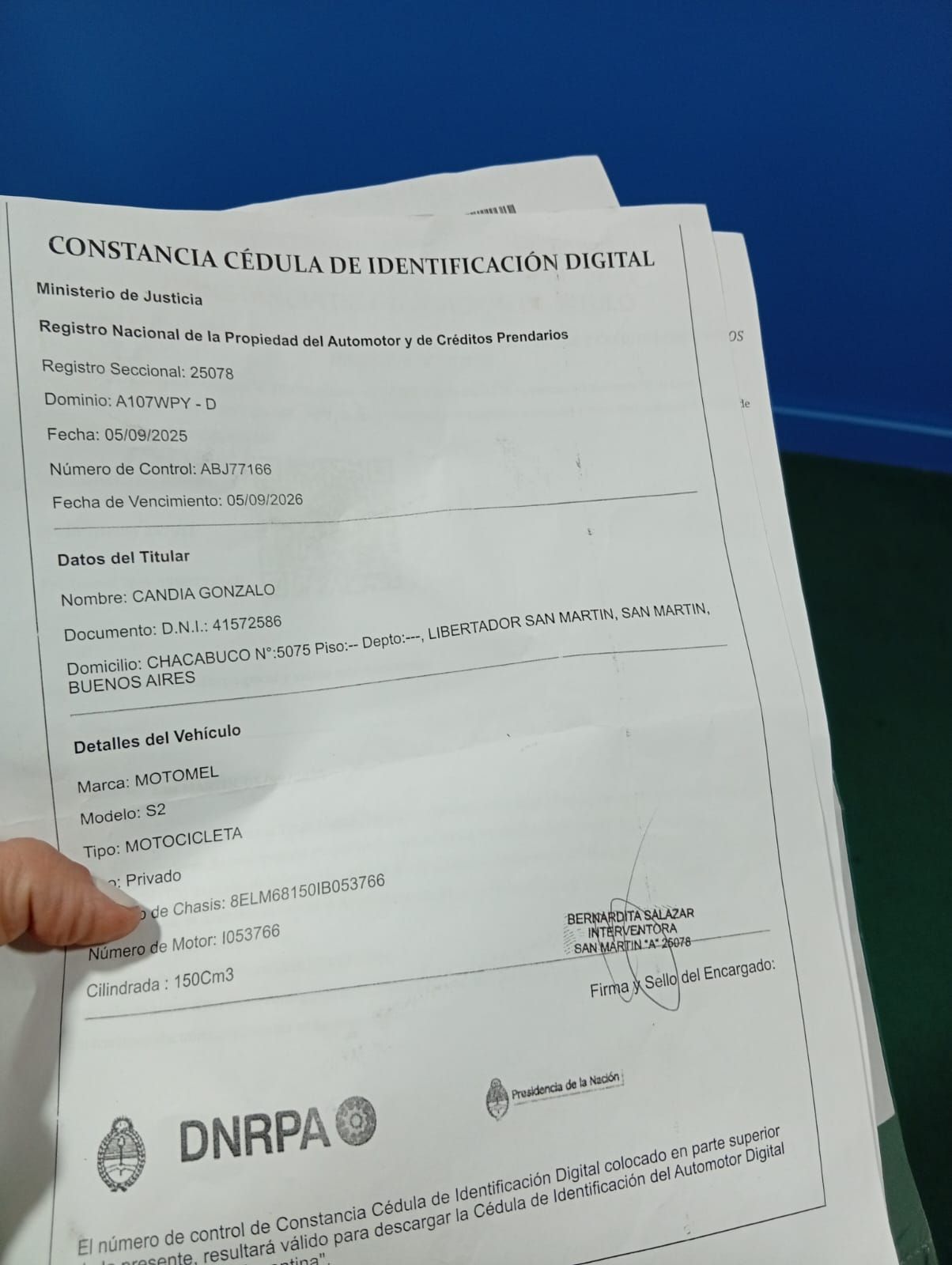 Una mano sostiene un formulario de papel con el logotipo de DNRPA sobre un escritorio azul.