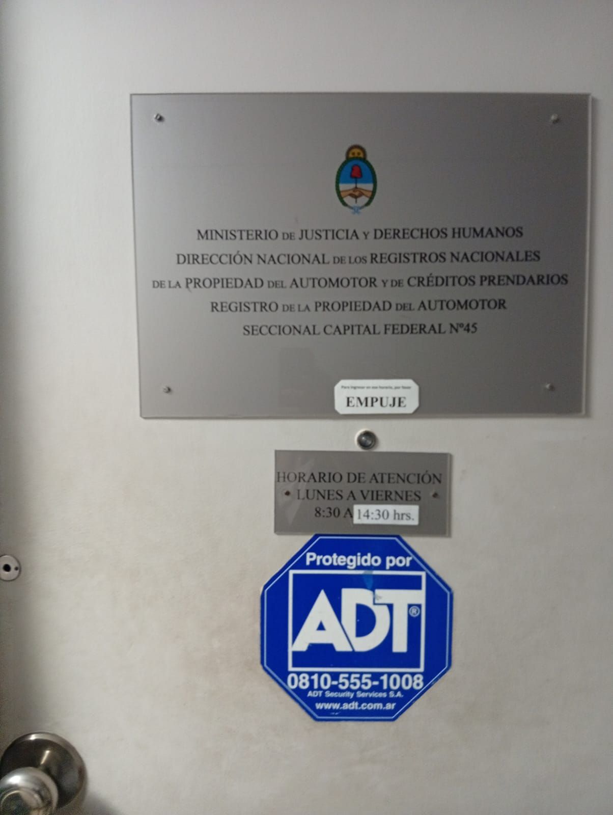 Placa en español en la pared, encima de una pegatina de seguridad de ADT y un pequeño letrero de metal.