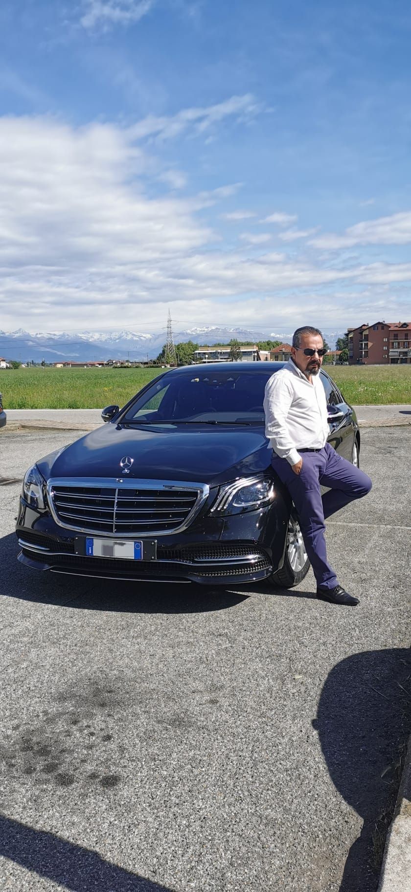 Un uomo è seduto sul cofano di un'auto in un parcheggio.