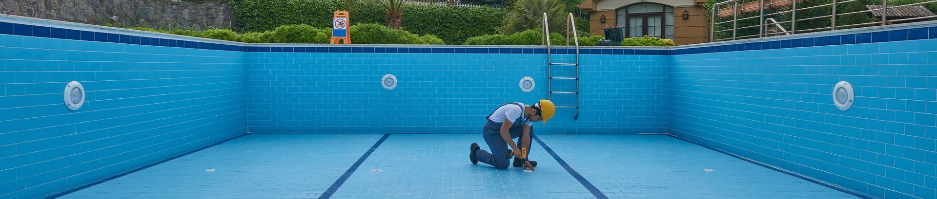 Empty swimming pool with white steps and blue mosaic tile liner. Concrete decking.