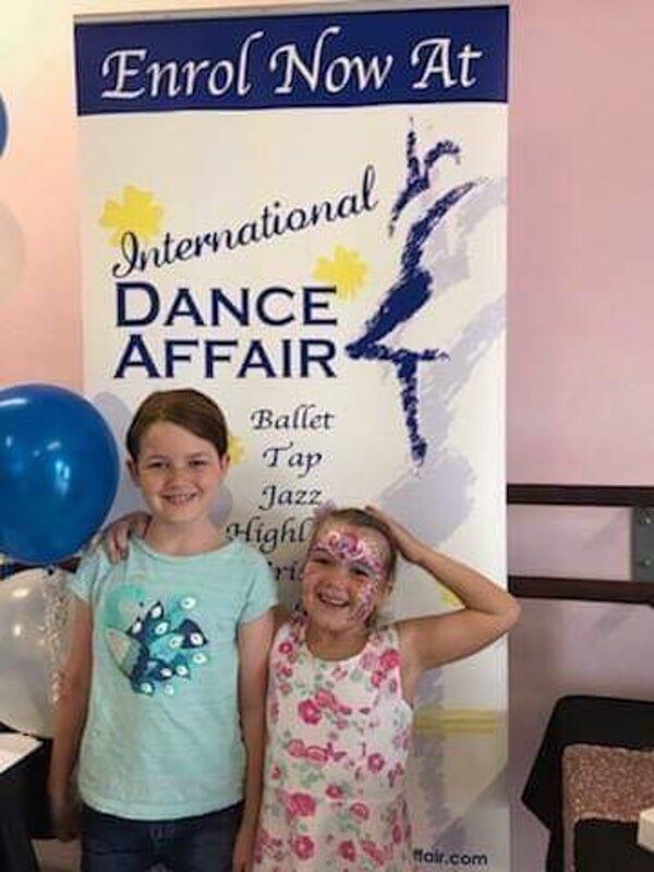 Two Young Girls Are Standing In Front Of A Sign — International Dance Affair In North Mackay, QLD