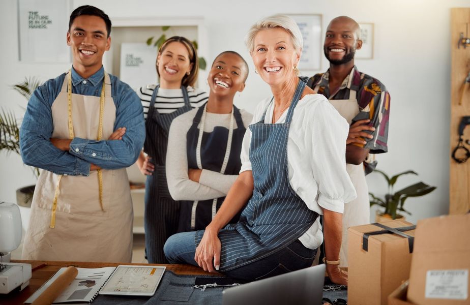 Group of people smiling, wearing aprons, in a brightly lit workshop or store.