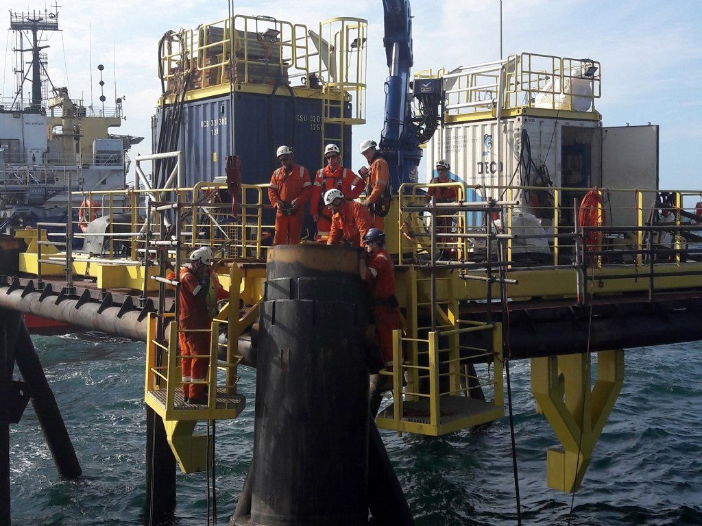 Workers in orange jumpsuits on offshore platform near a ship.