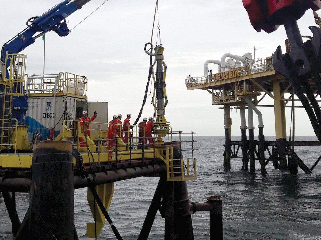 Oil rig workers in orange coveralls on a platform, rigging equipment above the ocean.