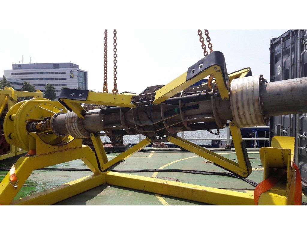 Yellow equipment holding a pipe on a deck. Chains suspend the equipment, building in the background.