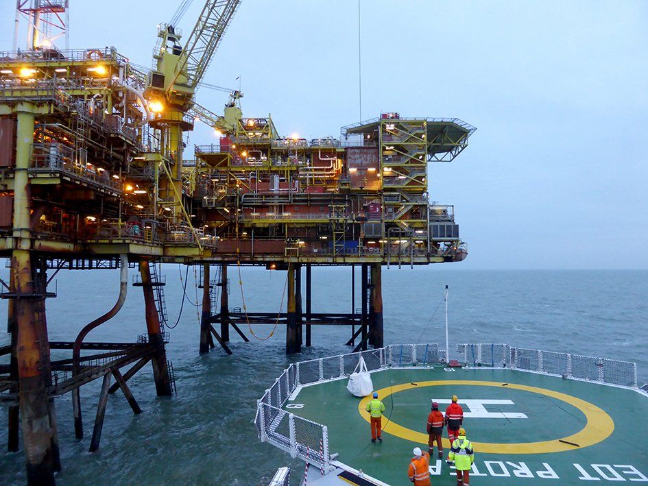 Offshore oil platform with helipad; workers in safety gear walk towards it.