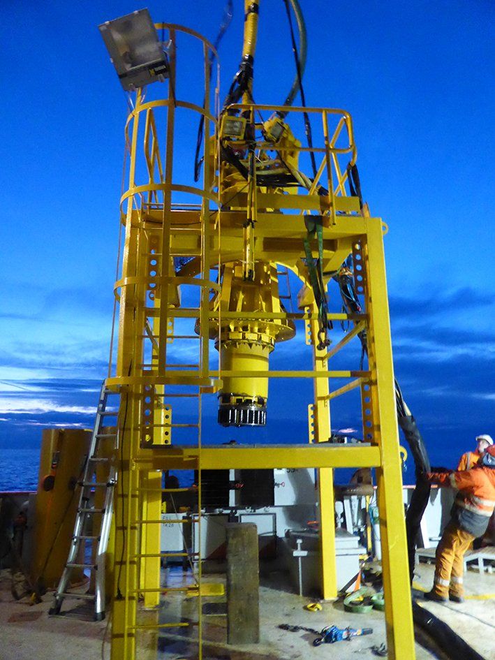 Yellow drilling equipment on a platform at night, with a worker in an orange jumpsuit.