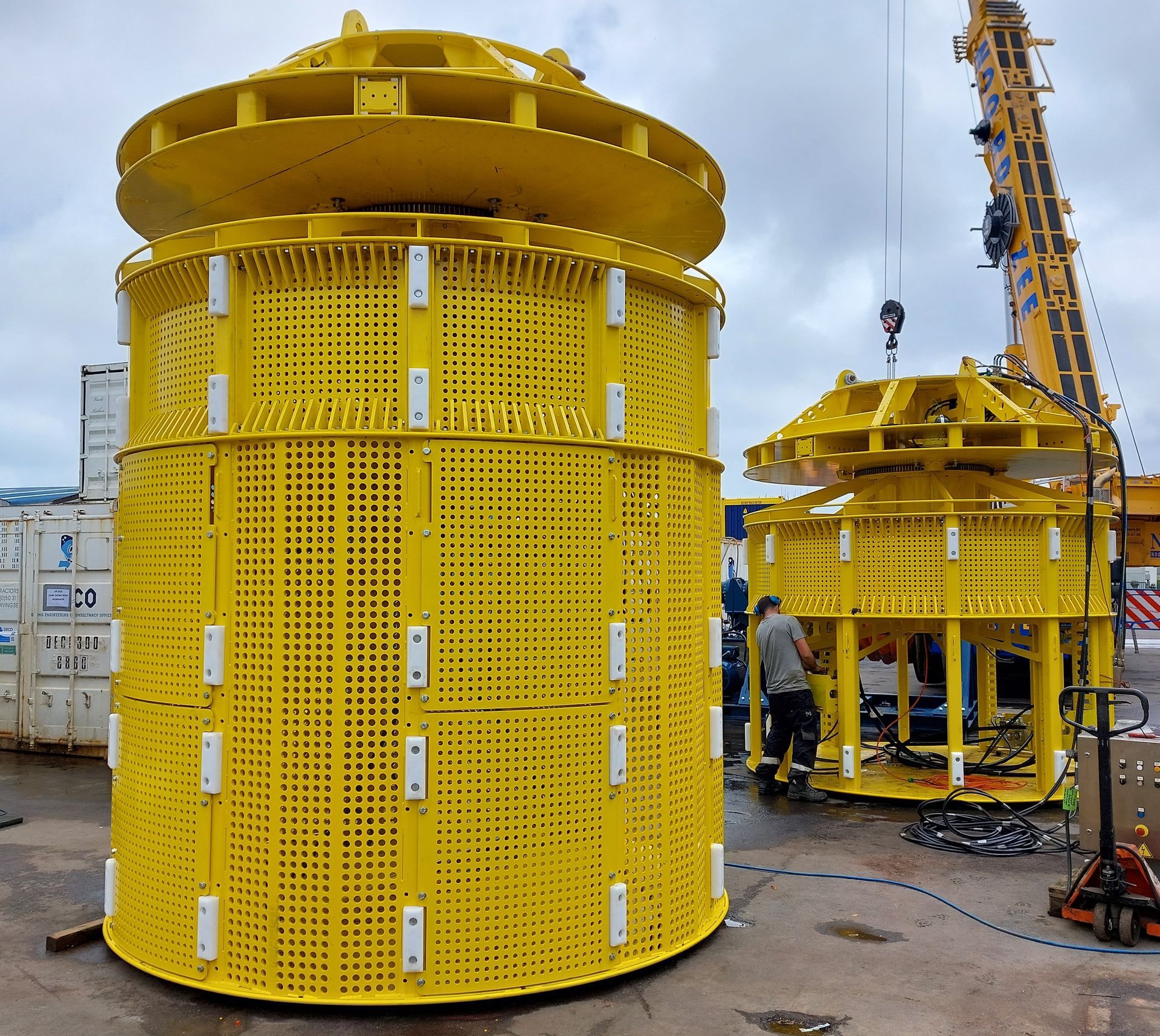 Two large yellow cylindrical structures with workers and a crane, outdoors.
