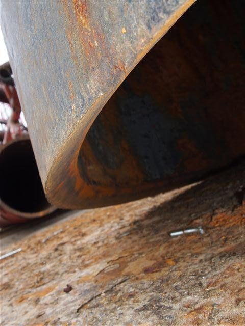 Rusty metal pipe resting on a weathered, rusty surface.