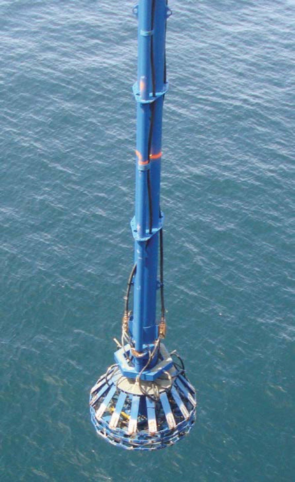 Blue industrial grab bucket lowered into ocean.