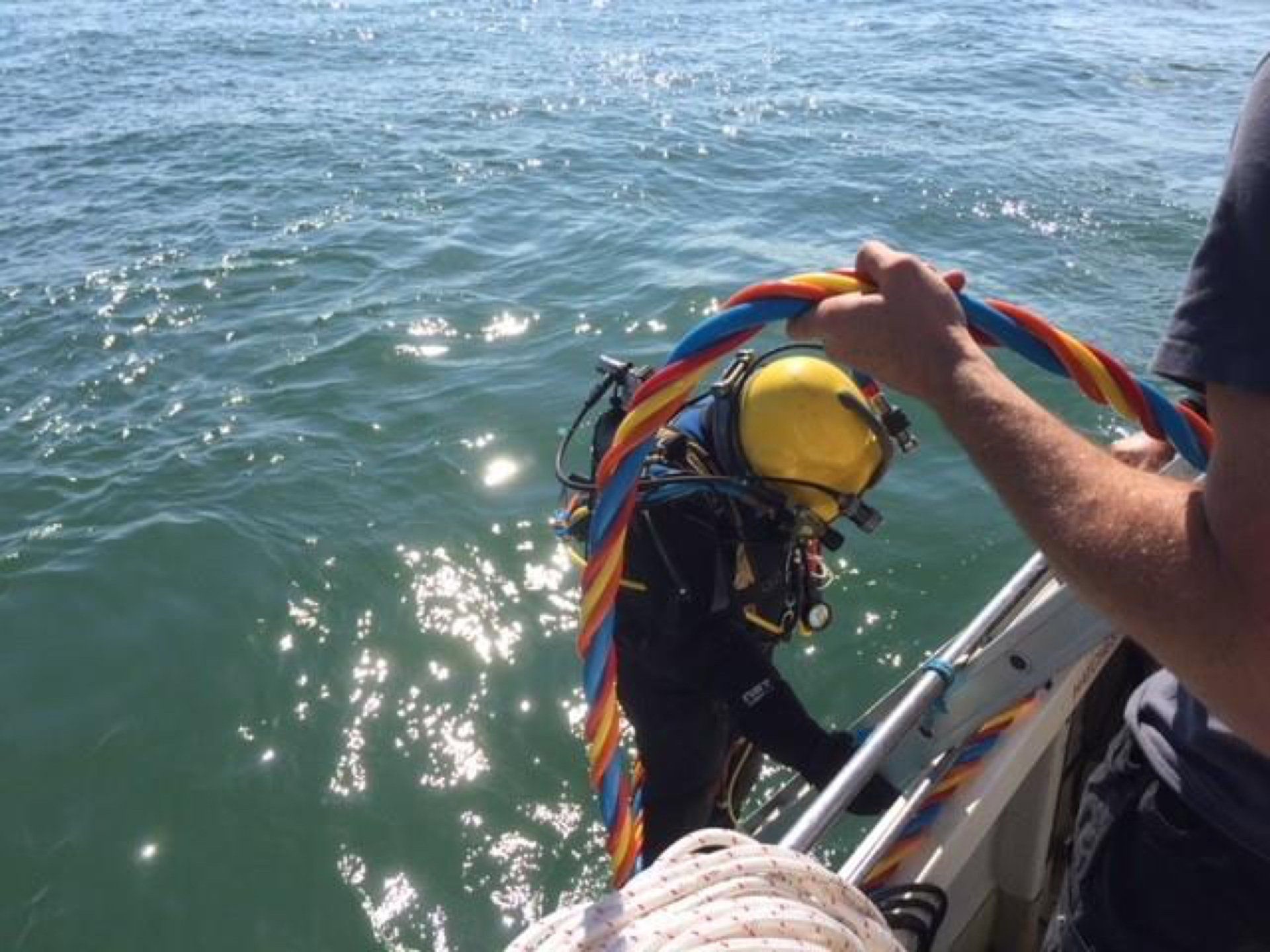 Scuba diver climbs a ladder from the sea onto a boat. Bright sun on water.
