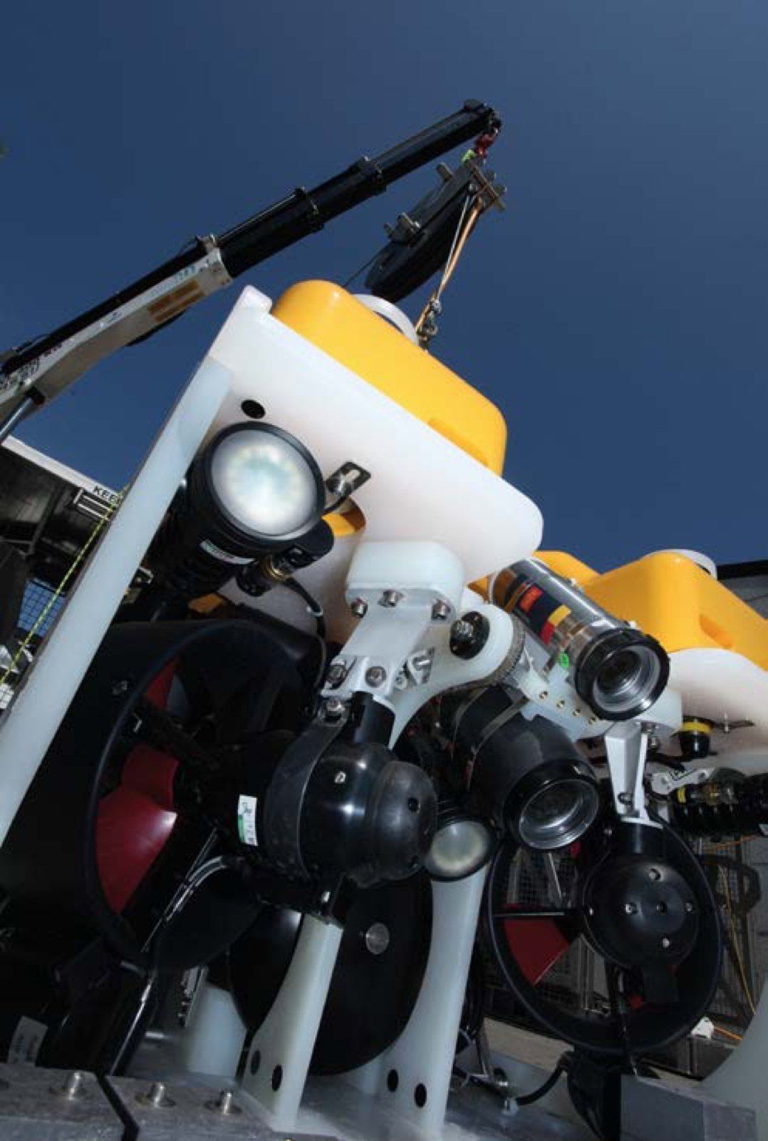 Underwater robot ROV with bright lights, being lowered by a crane, against a blue sky.