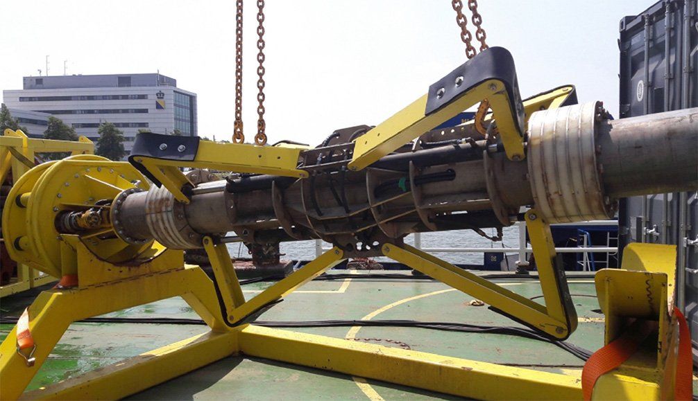 Yellow machinery securing a pipe section, likely for subsea work, outdoors.