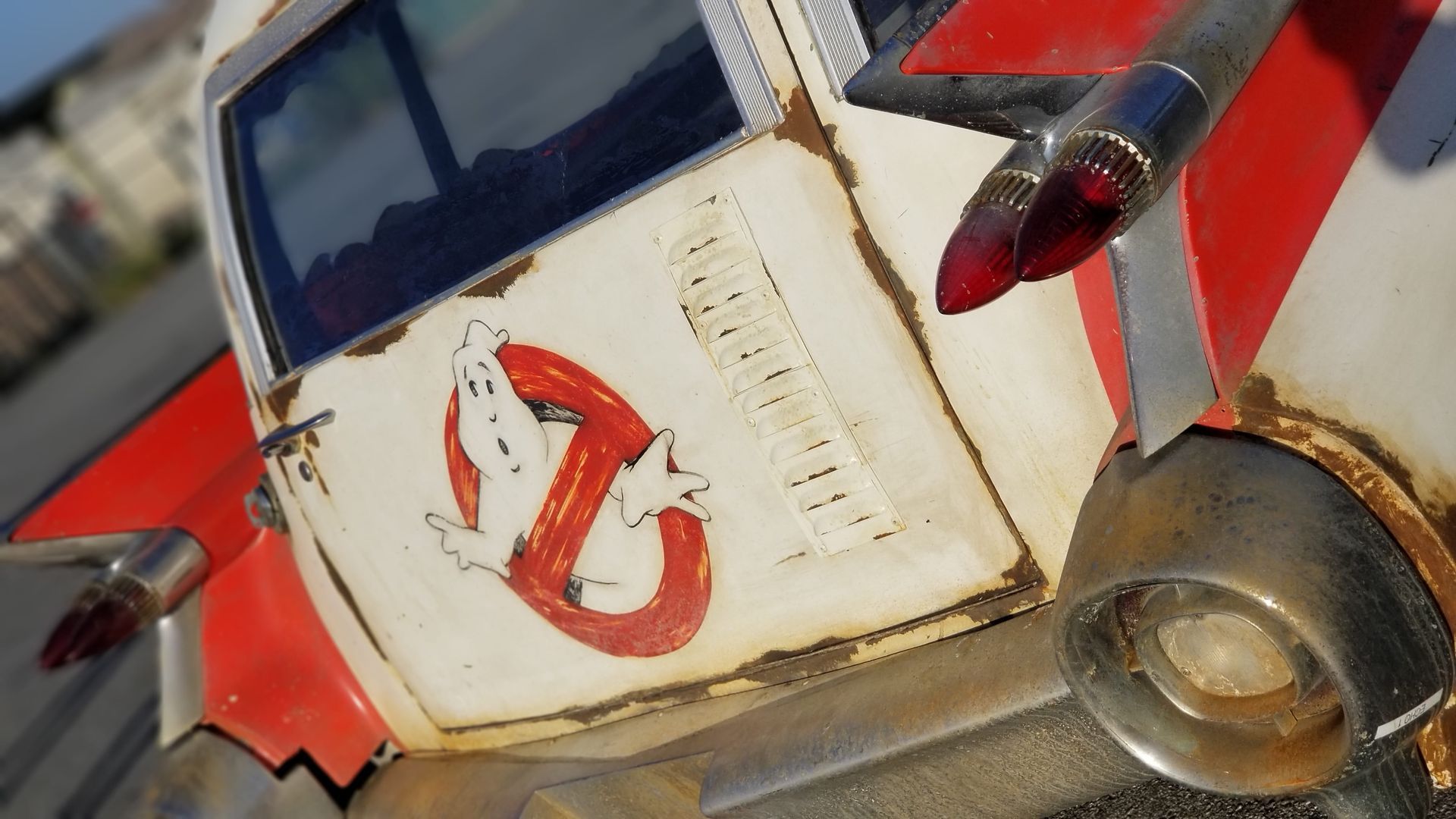 Ghostbusters Ecto-1 car with logo, red and white, aged appearance.