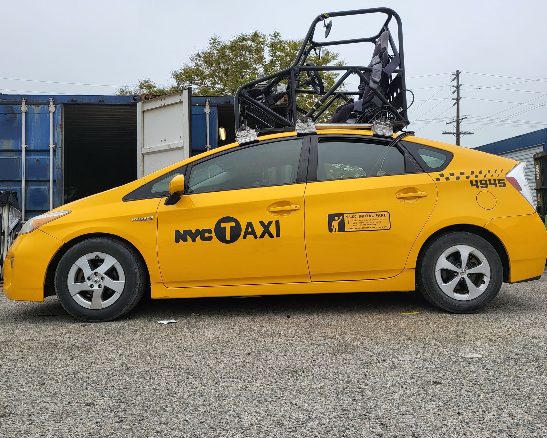 A yellow taxi cab is parked in front of a chain link fence and ready to install a pod rig for film shooting.
