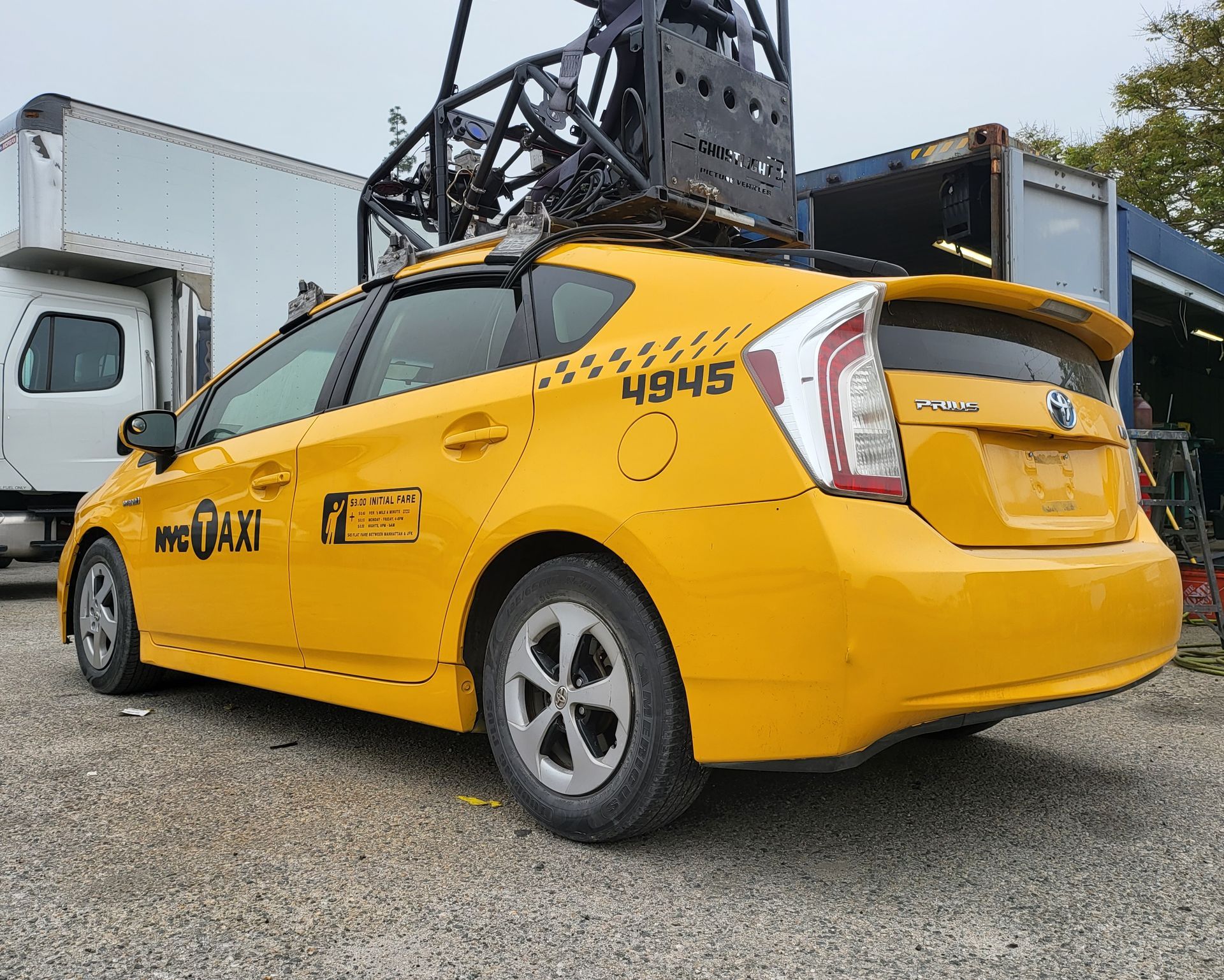 A yellow taxi cab is parked in front of a chain link fence and ready to install a pod rig for film shooting.