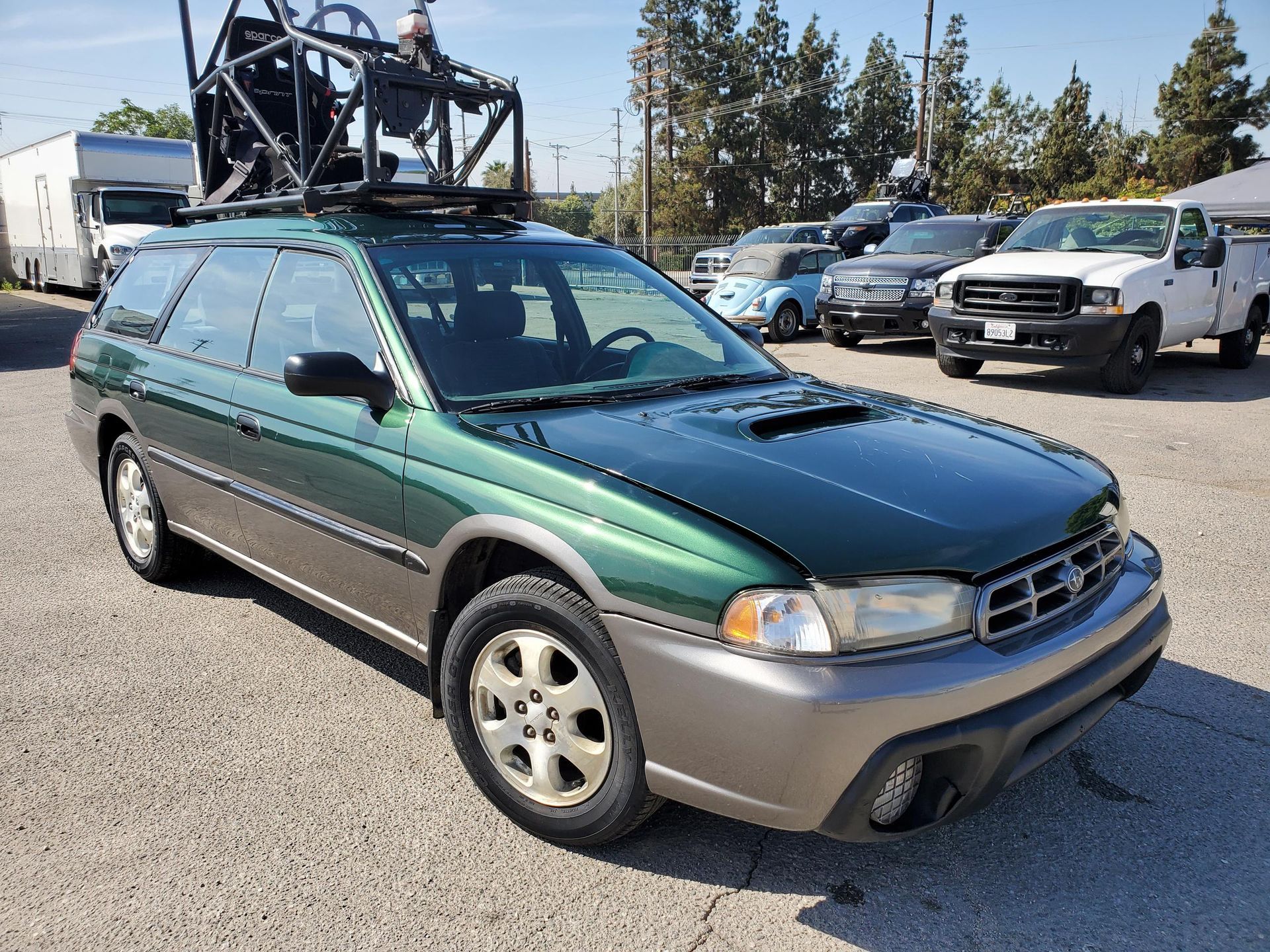 A green Subaru station wagon is parked on the side of the road with installed pod rigs on it for film shooting.