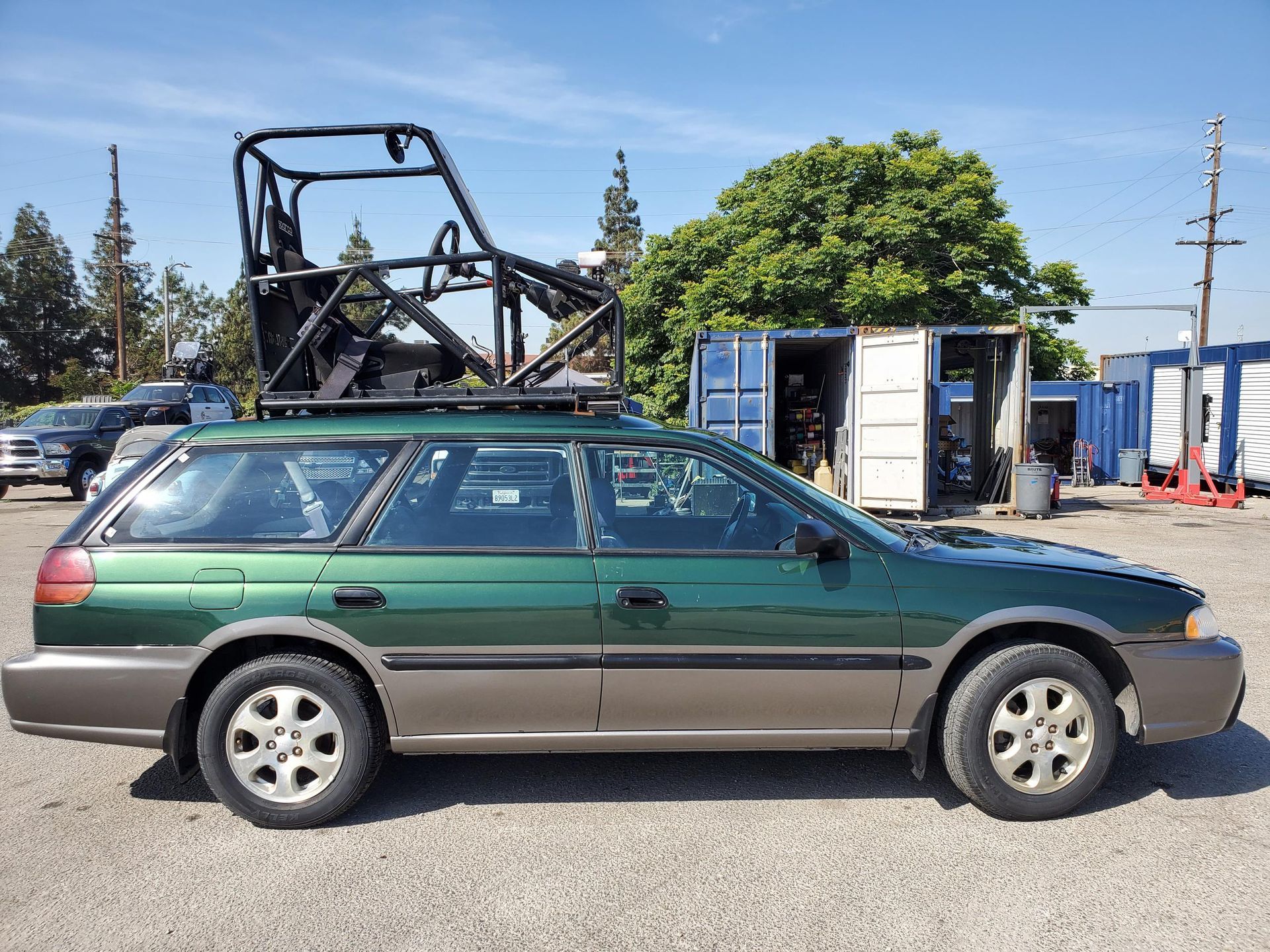 A green Subaru station wagon is parked on the side of the road with installed pod rigs on it for film shooting.