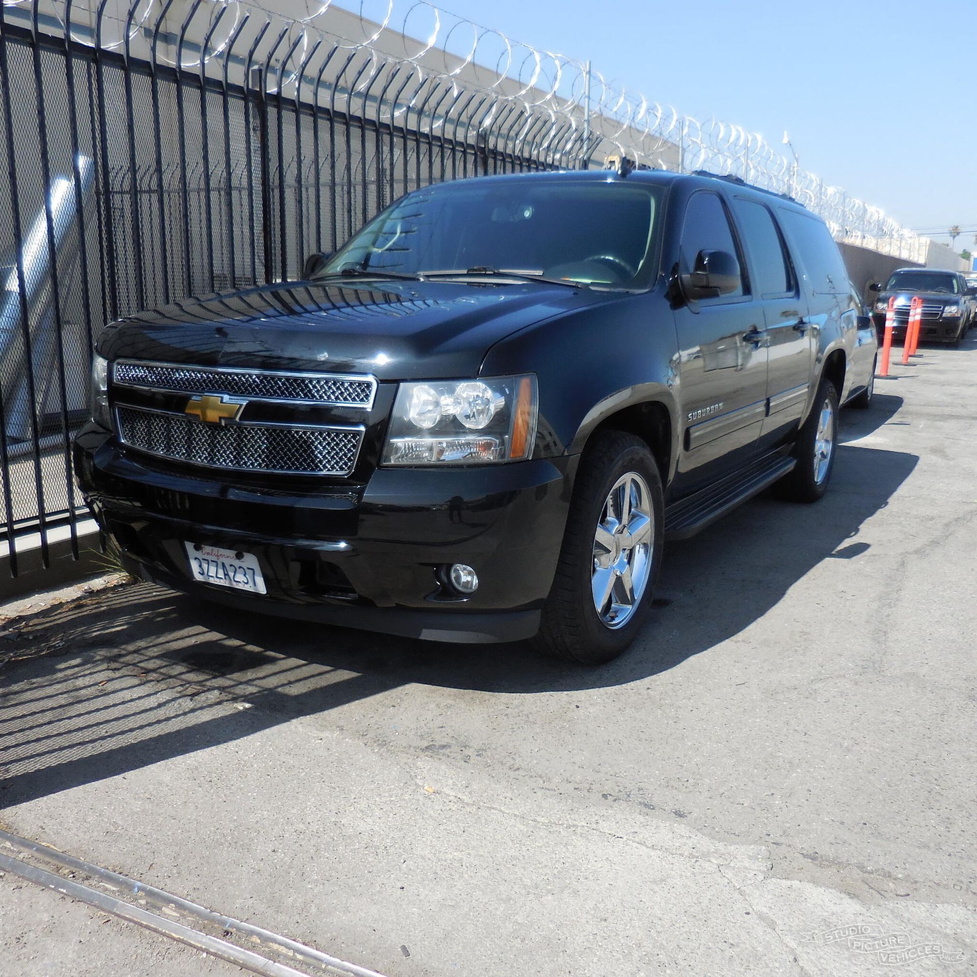 a black suv is parked in front of a fence and ready to install a pod rig for film shooting.