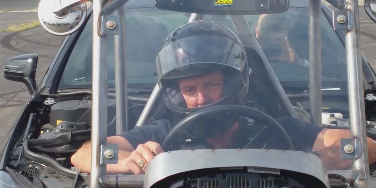 A man wearing a helmet is focused on driving a car, showcasing safety and concentration on the road.