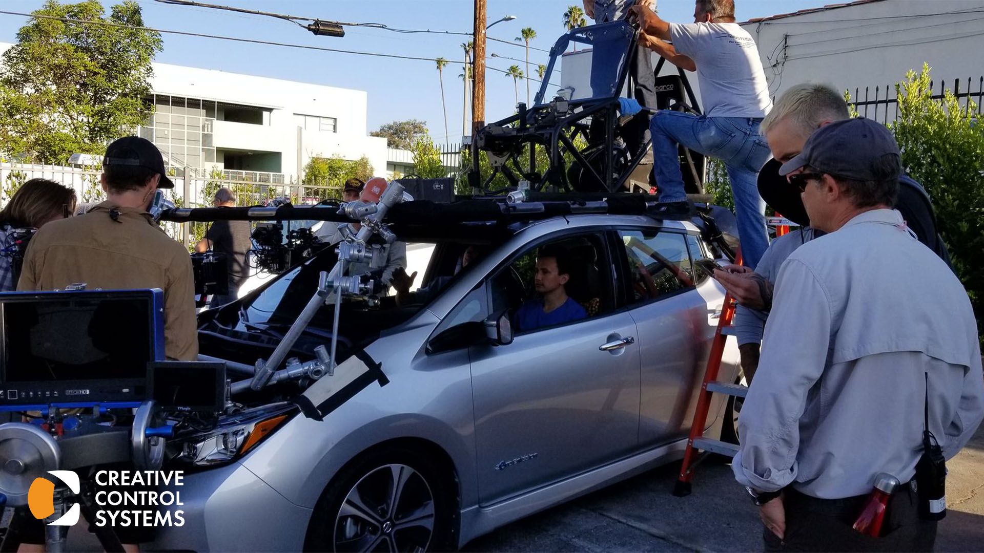 A group of individuals gathered around a car equipped with a camera mounted on its roof.