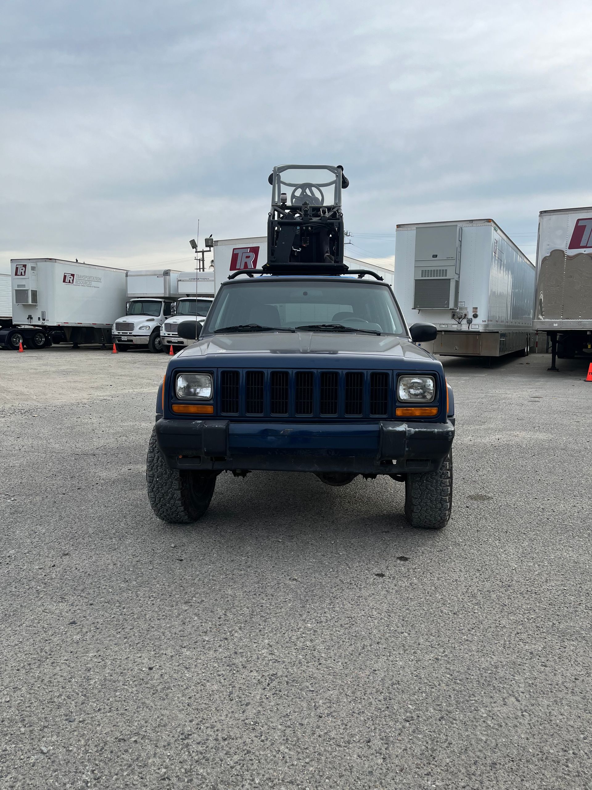A blue jeep with a forklift on top of it is parked in a gravel lot with pod rigs installed on it for film shooting.