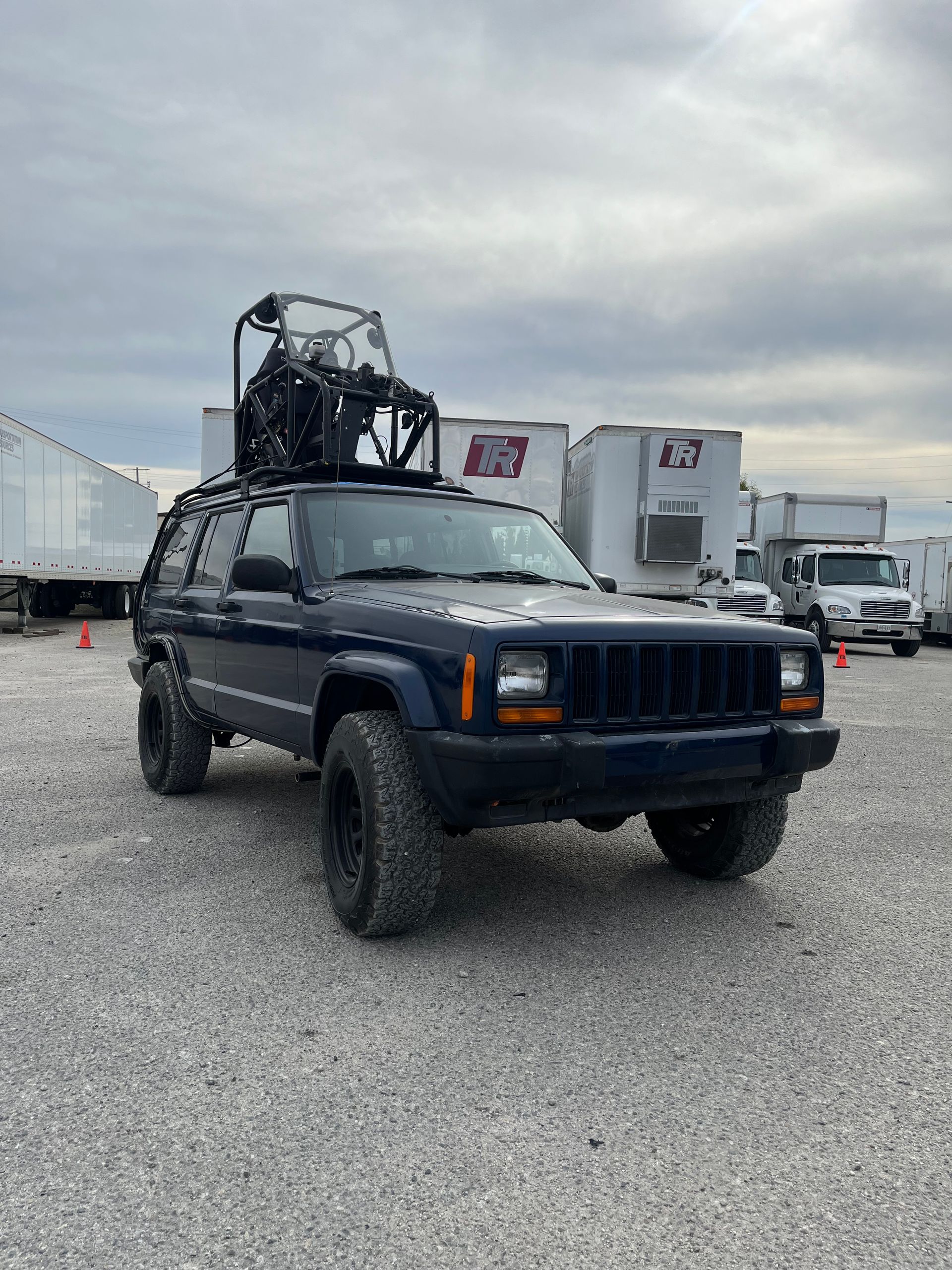 A blue jeep with a forklift on top of it is parked in a gravel lot with pod rigs installed on it for film shooting.