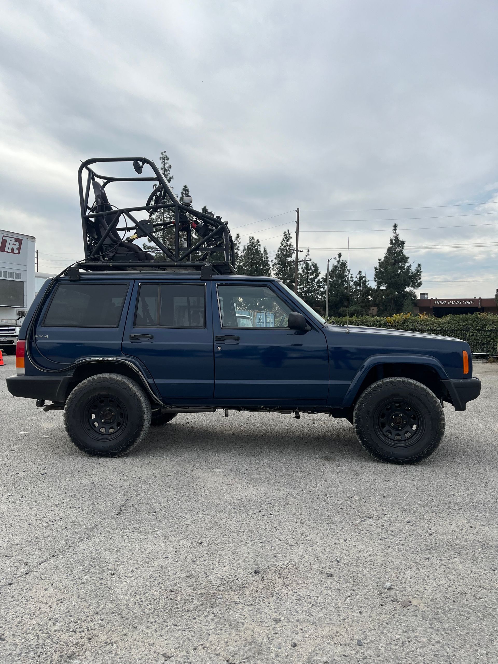A blue jeep with a forklift on top of it is parked in a gravel lot with pod rigs installed on it for film shooting.