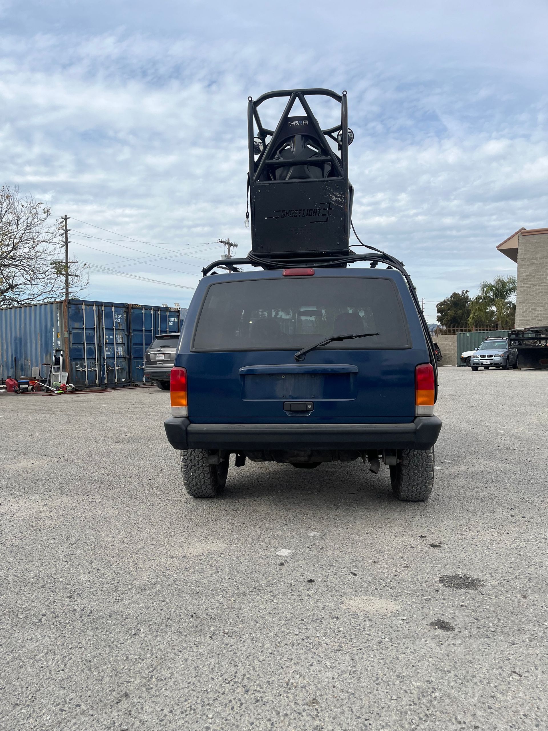 A blue jeep with a forklift on top of it is parked in a gravel lot with pod rigs installed on it for film shooting.