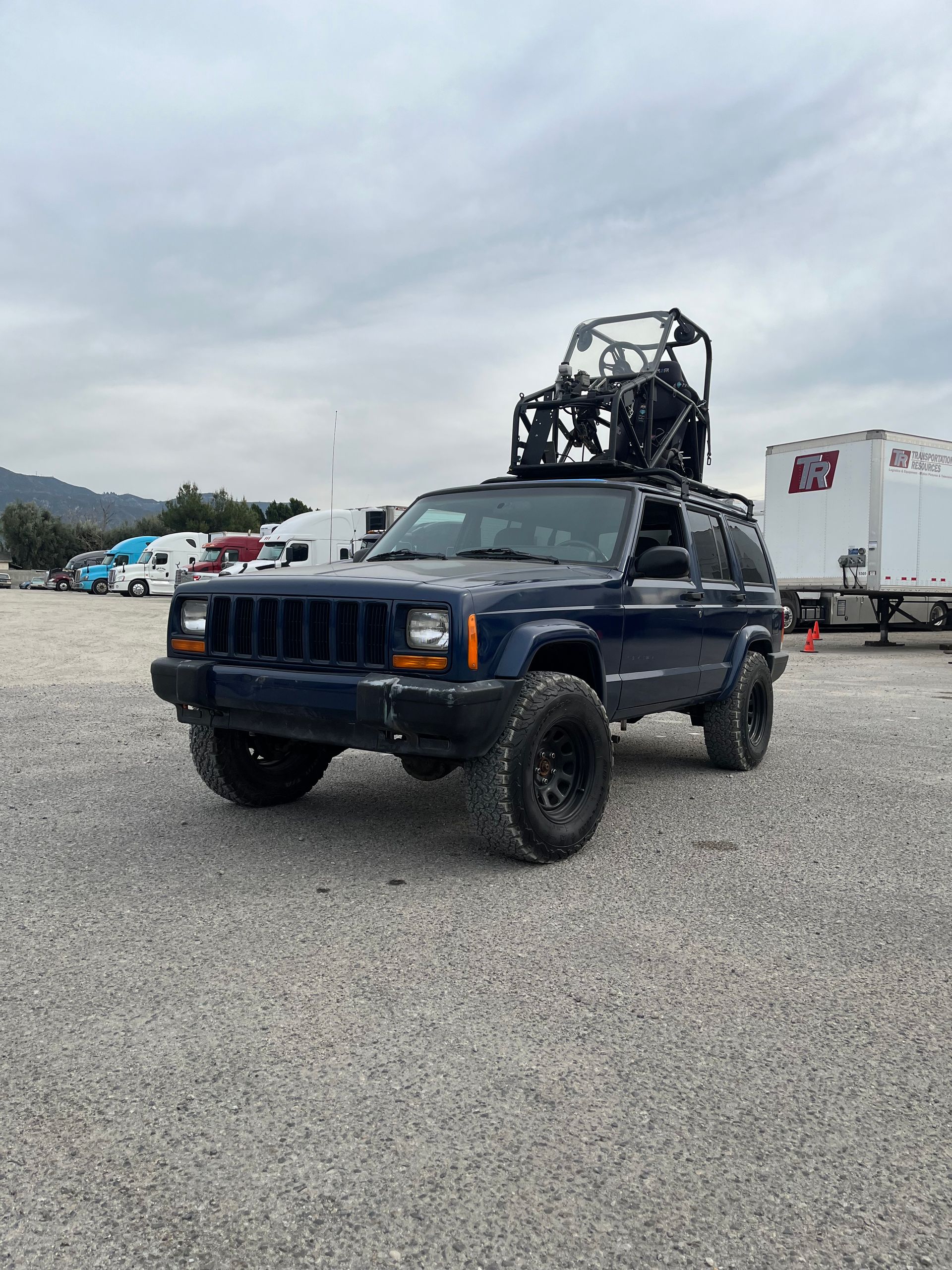 A blue jeep with a forklift on top of it is parked in a gravel lot with pod rigs installed on it for film shooting.