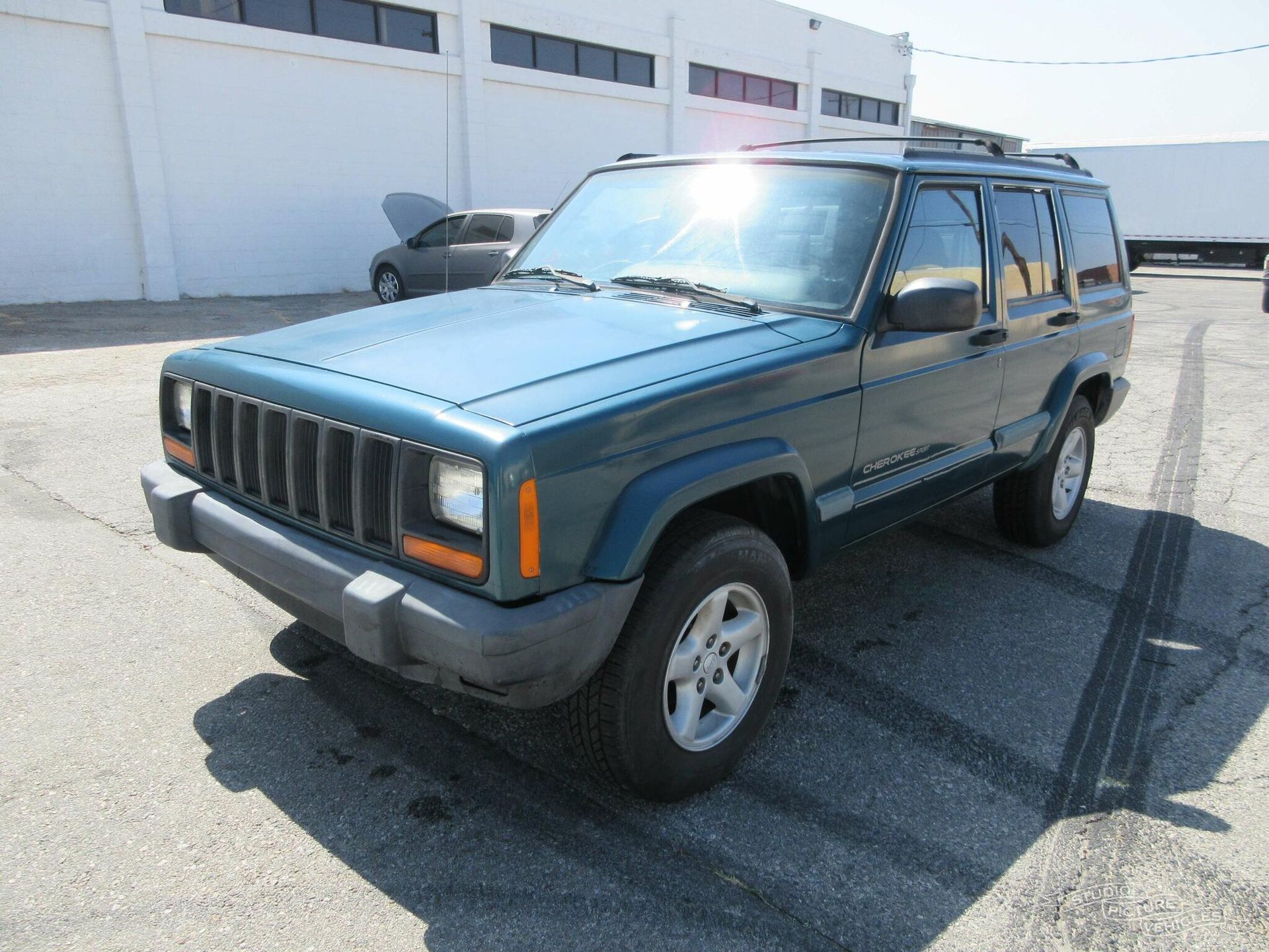 a blue jeep cherokee is parked in front of a white building and ready to install a pod rig for film shooting.