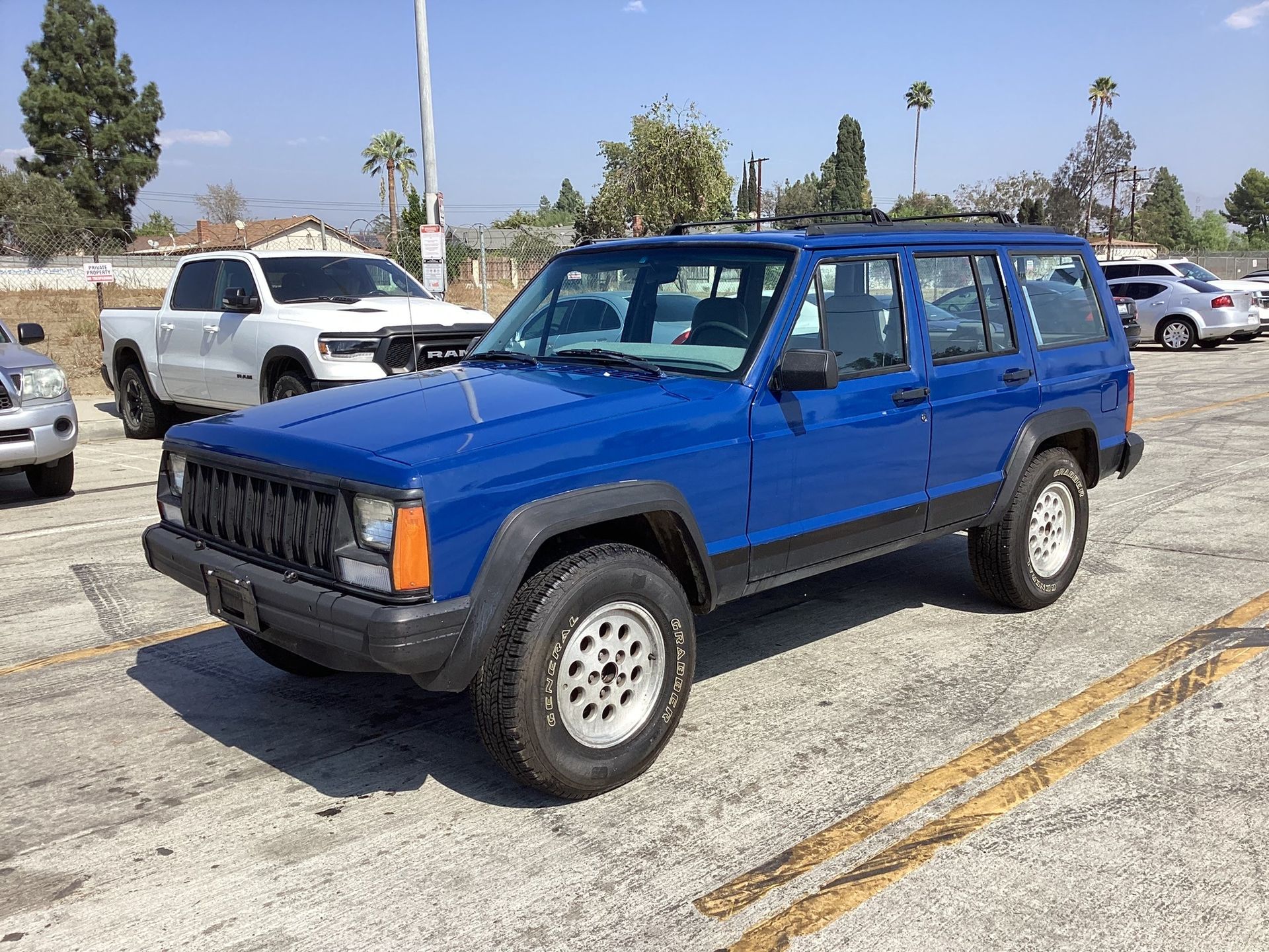 a blue jeep cherokee is parked in a parking lot next to a white truck and ready to install a pod rig for film shooting.