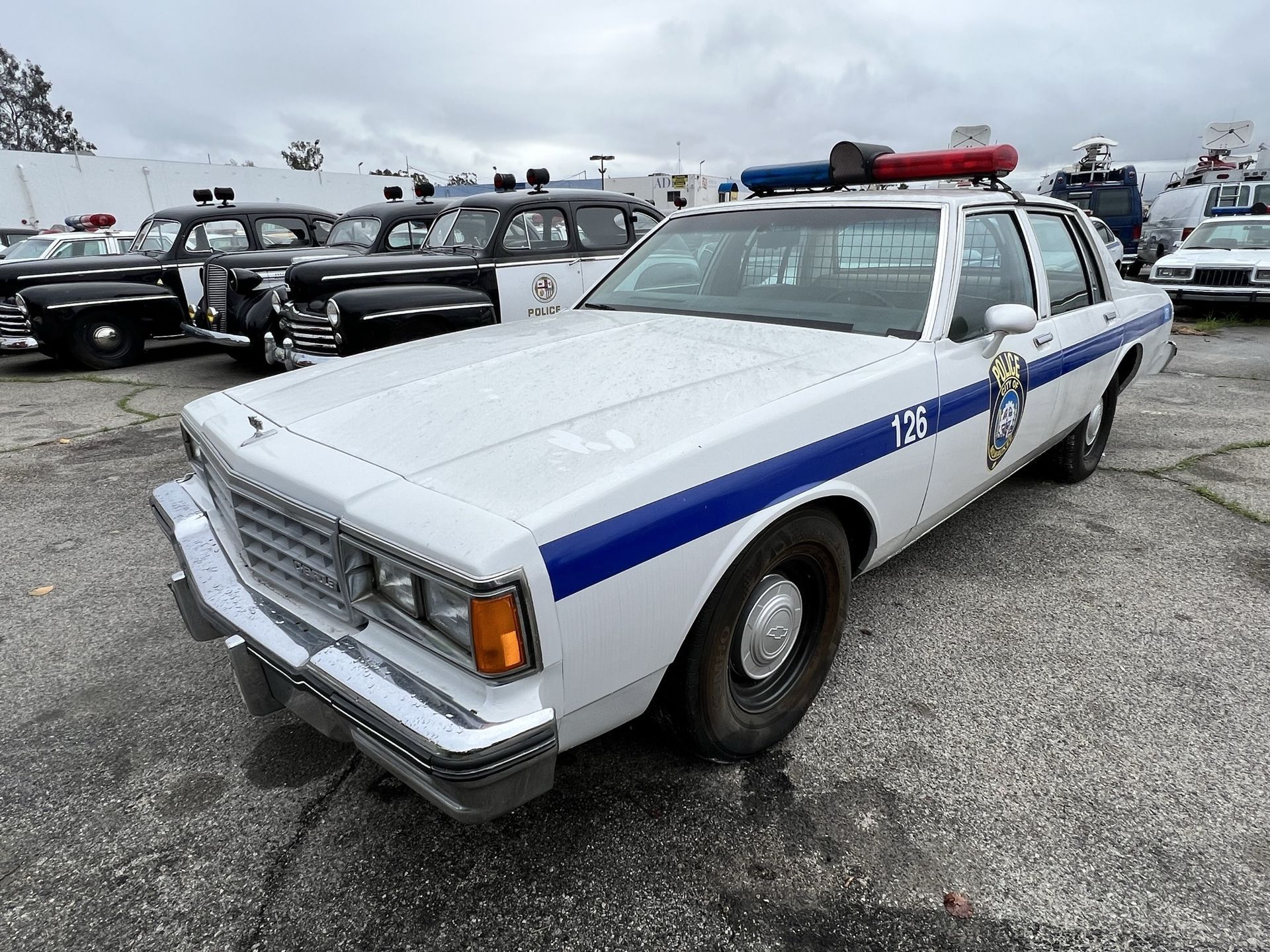 a white and blue police car is parked in a parking lot  and ready to install a pod rig for film shooting.