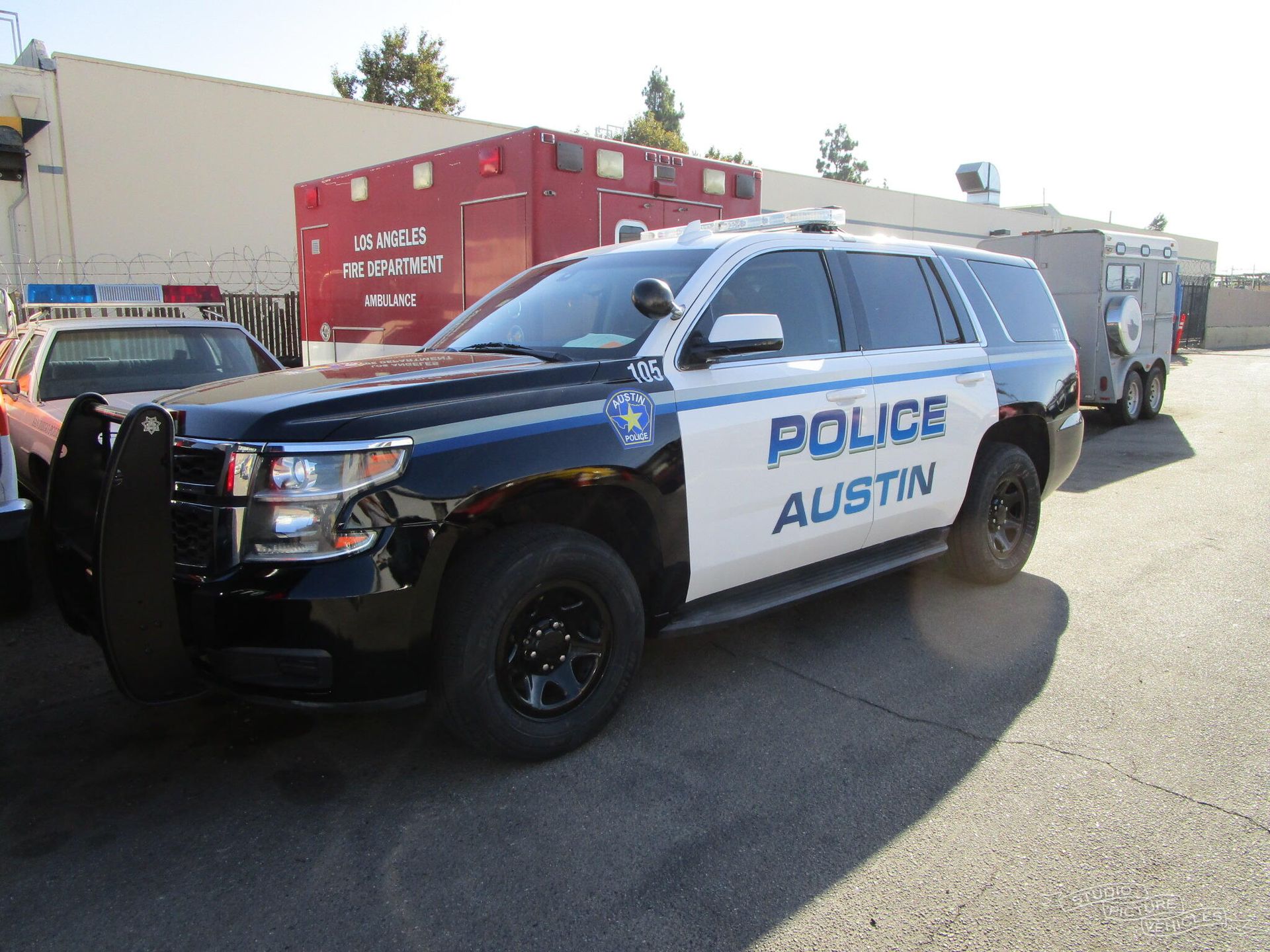 a white suv with a police light on top of it is parked in front of a barbed wire fence  and ready to install a pod rig for film shooting.