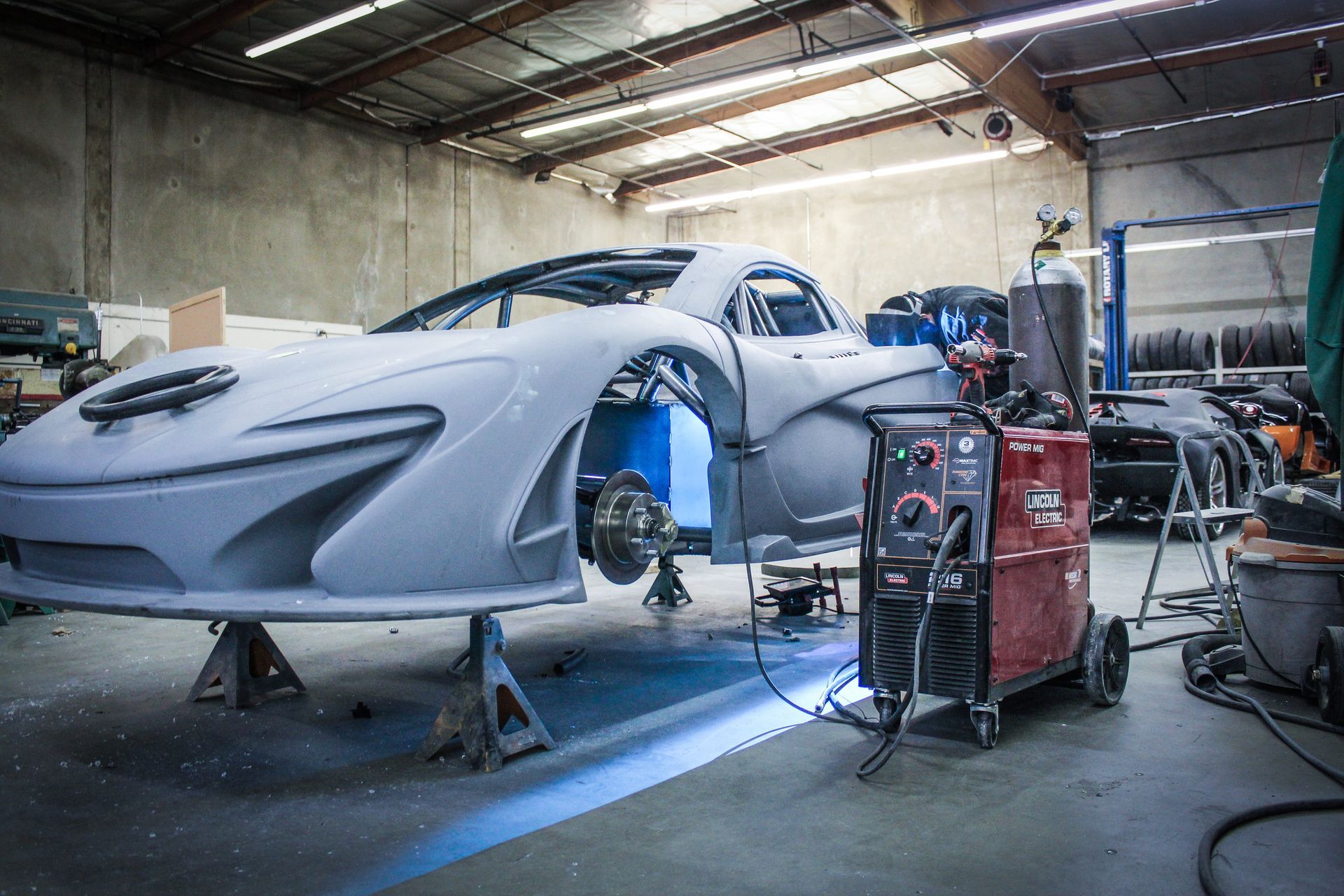 Need for Speed car - A partially built gray sports car inside a workshop, with welding equipment in front.