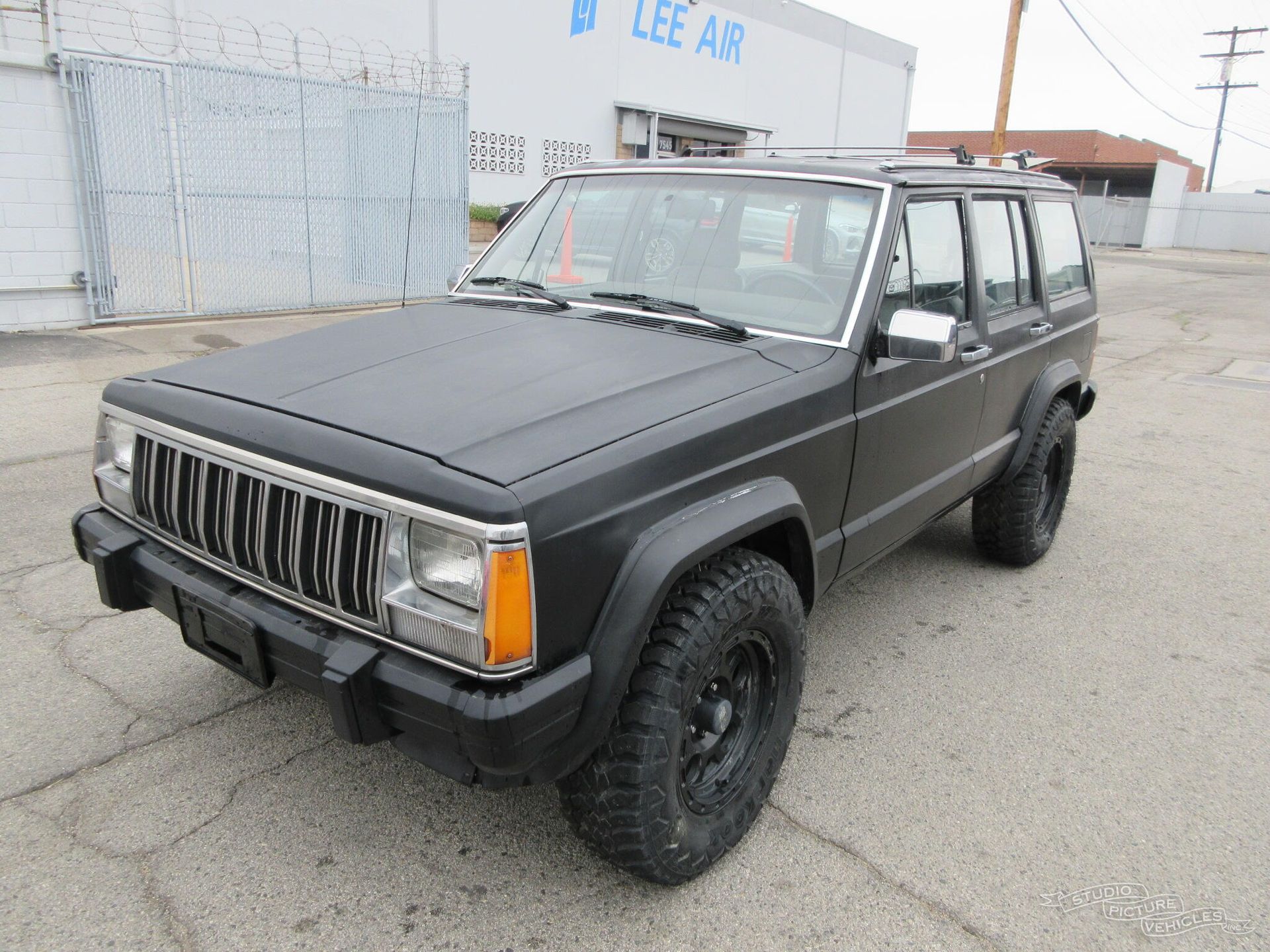 a black jeep cherokee is parked in front of a building and ready to install a pod rig for film shooting.