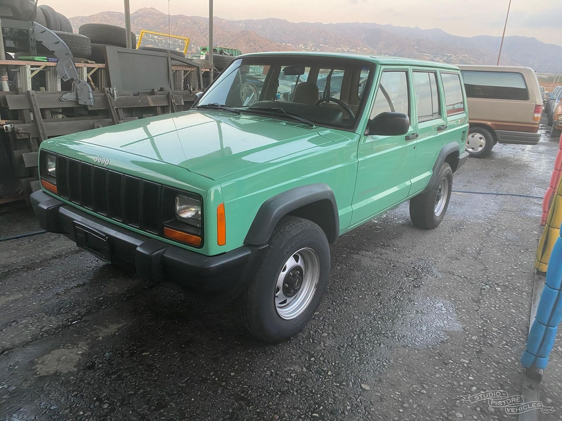 a green jeep is parked in a parking lot next to a pile of tires and ready to install a pod rig for film shooting.