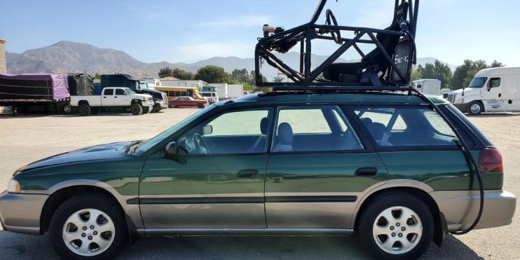 A green car featuring a roof rack on top, parked against a scenic backdrop.