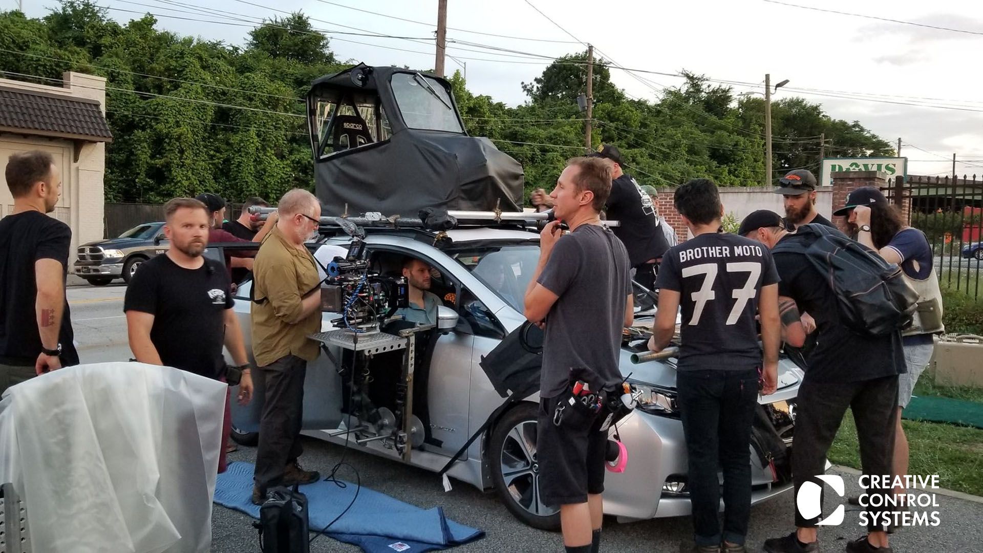 A group of individuals gathered around a car, capturing moments with a camera, showcasing teamwork and creativity in action.
