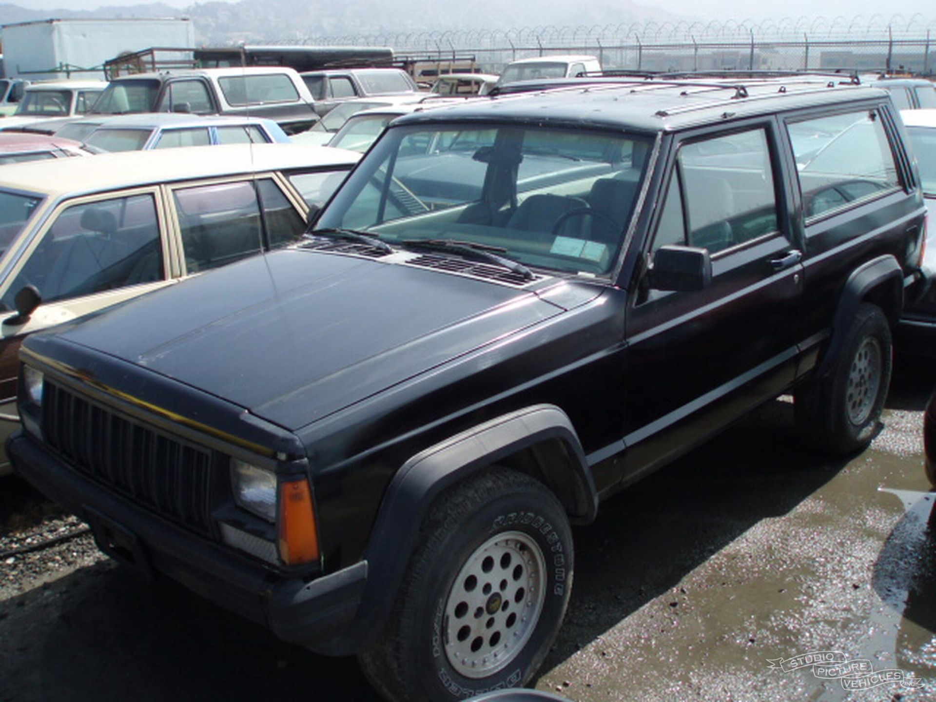 a black jeep is parked in a lot with other cars and ready to install a pod rig for film shooting.