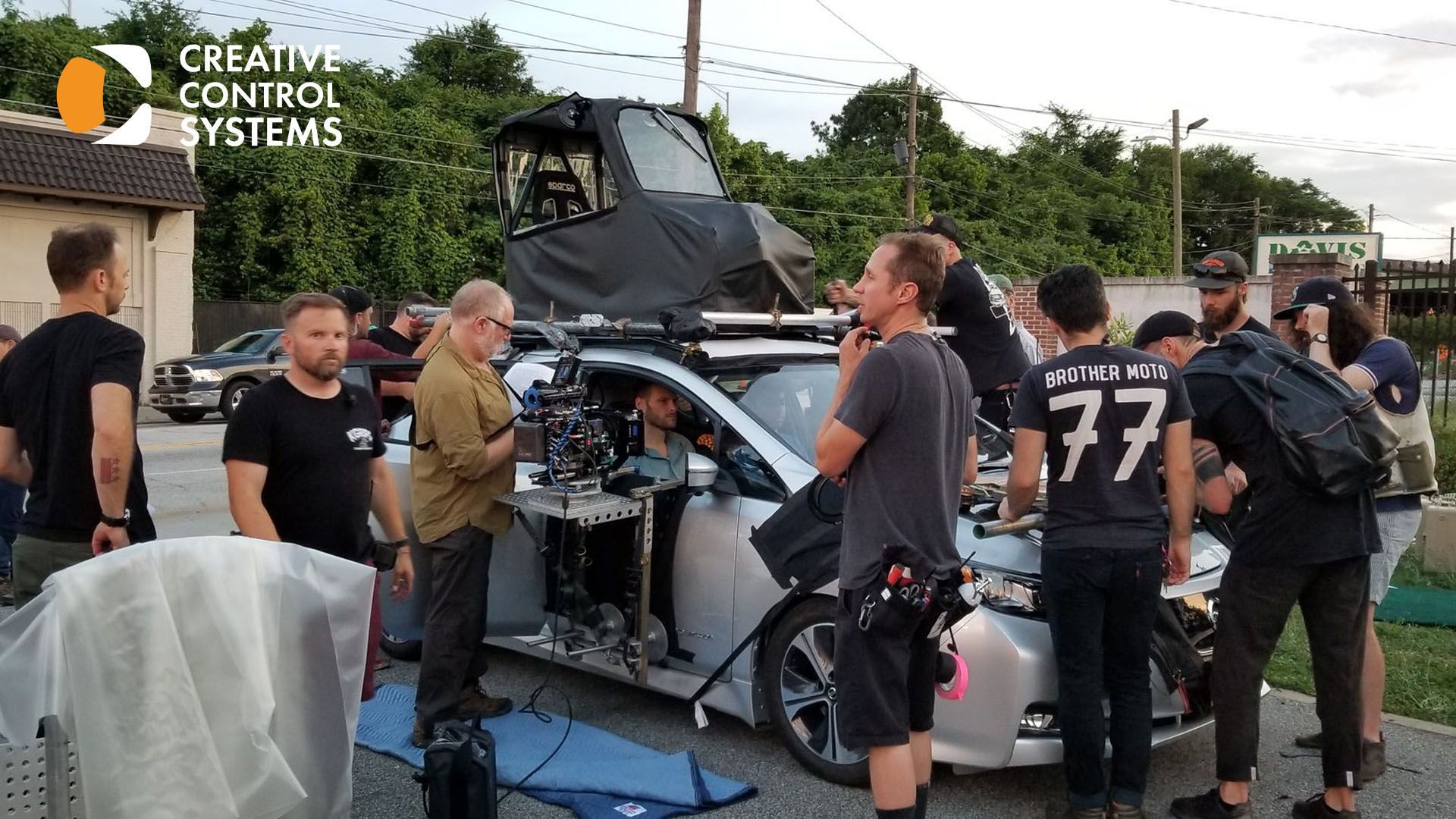 A group of individuals gathered around a car equipped with a camera mounted on its roof.